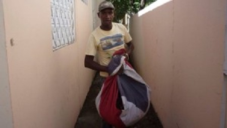 Tal si fuera una funda o un saco cualquiera, este ciudadano utiliza el paño tricolor dominicano para carga basura del patio del Centro Regional de Bienes Nacionales en San Juan de la Maguana.